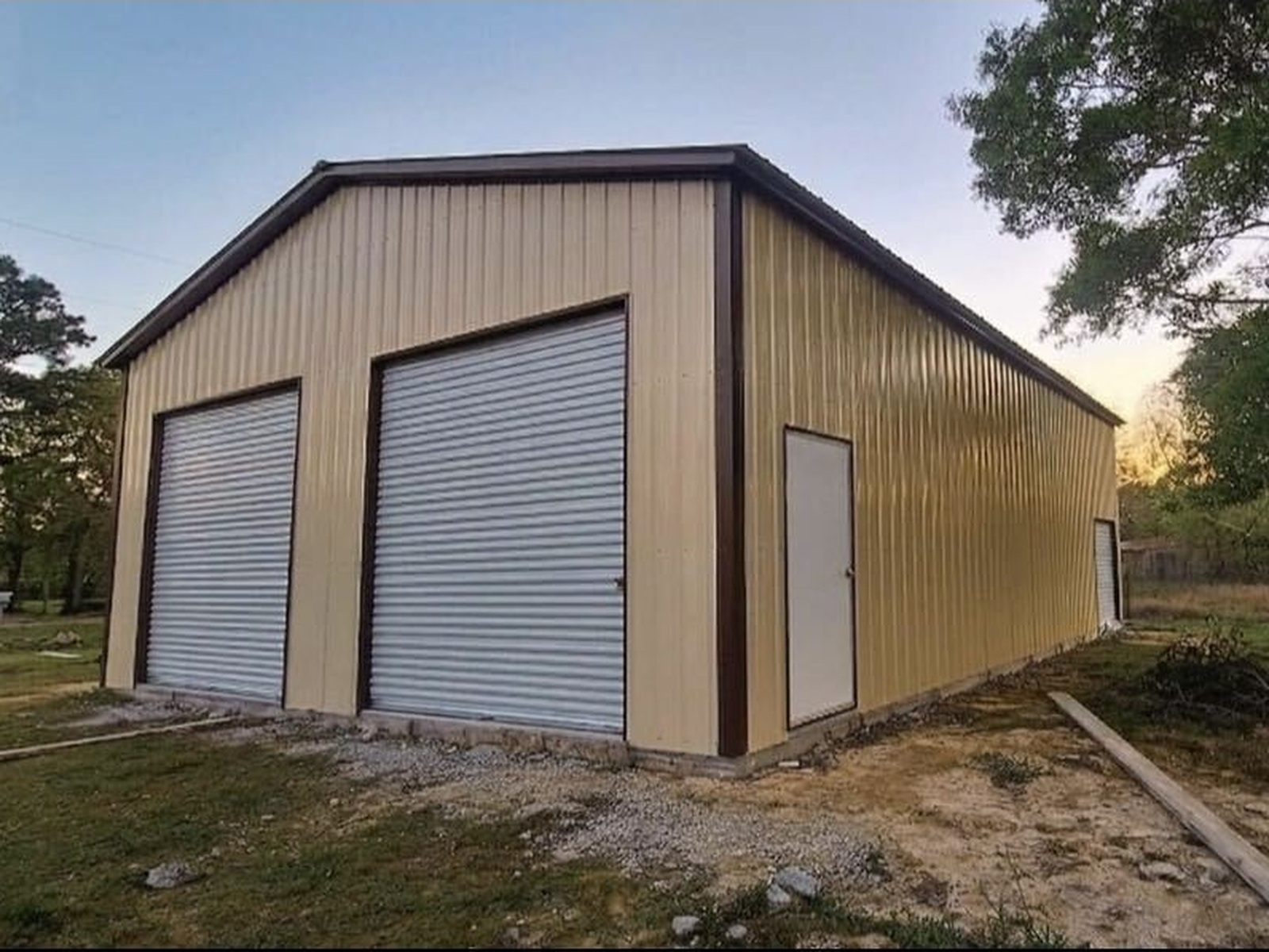 Tan metal garage with brown trim, two roll-up doors, a side door, and a tree on the right — a Forge Steel job